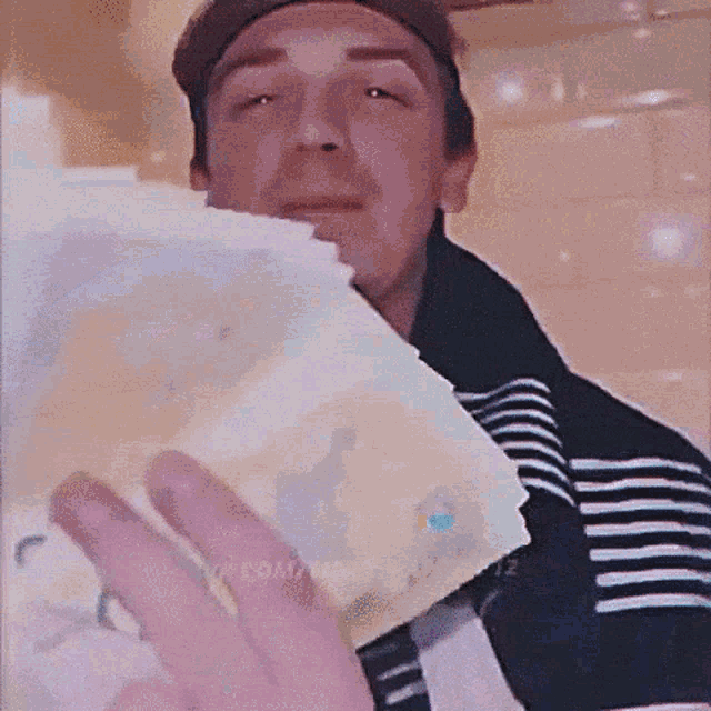 a man in a striped shirt is holding a piece of paper in front of his face .