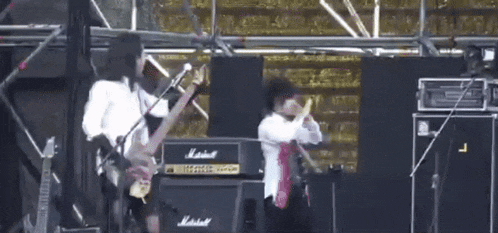 a man is playing a guitar while another man sings into a microphone on stage .