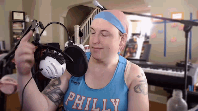 a man wearing a blue philly tank top is standing in front of a microphone