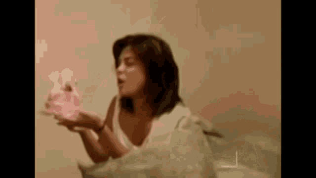 a woman is blowing out candles on a cake while sitting on a bed .