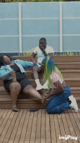 a group of people are sitting on a wooden bench and one of them is kneeling down to touch another person 's foot