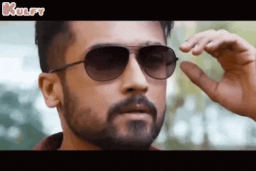 a man with a beard is wearing sunglasses and making a gesture with his hand .