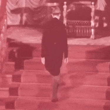 a man is walking down a red carpet towards a throne in a room .