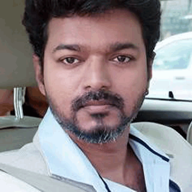 a man with a beard is sitting in a car and taking a selfie .