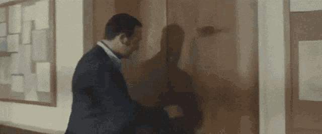 a man in a suit is shaking hands with another man in front of a bulletin board .
