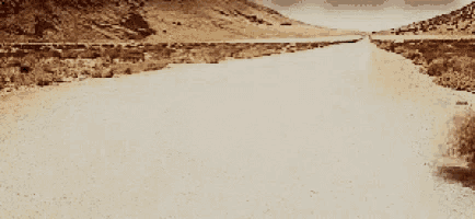 a dirt road going through a desert with mountains in the background .