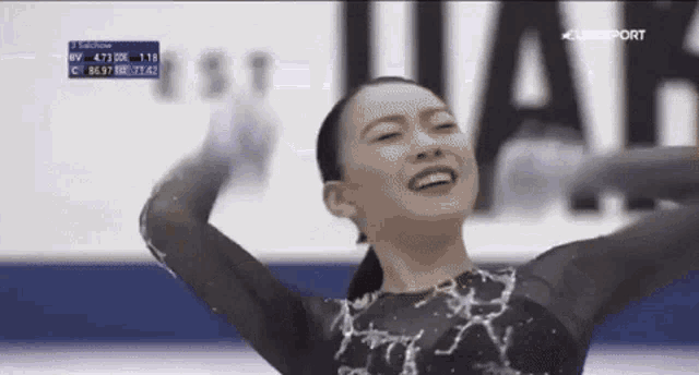 a female figure skater is smiling with her hands in the air .