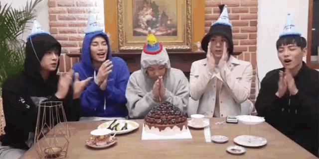 a group of young men wearing party hats are sitting at a table with a birthday cake
