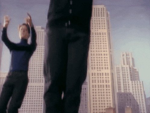 a blurry picture of two men dancing in front of tall buildings