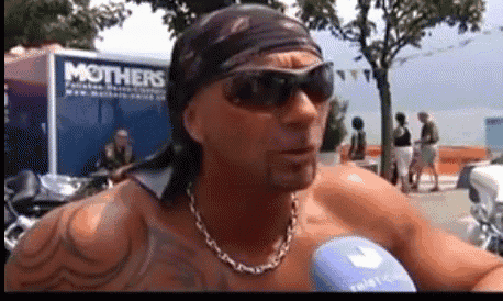 a man wearing sunglasses and a bandana stands in front of a mothers trailer
