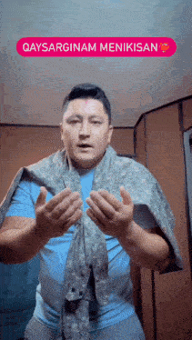 a man wearing a blue shirt and a scarf around his neck is making a gesture with his hands .