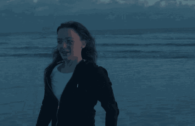 a woman in a black hoodie is standing on a beach