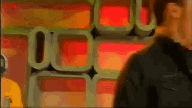 a man in a black jacket and a white shirt is smiling in front of a wall of red and orange boxes .