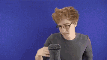 a young man wearing glasses is scratching his head in front of a microphone .