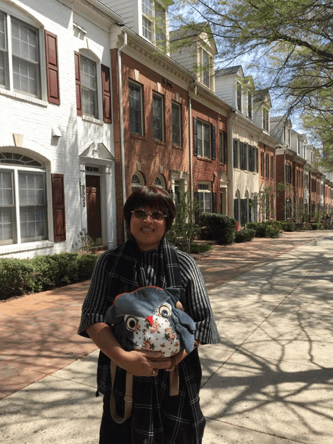 a woman holding a stuffed animal in front of a row of houses with shutters