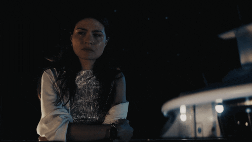 a woman in a white jacket and silver top is standing in the dark