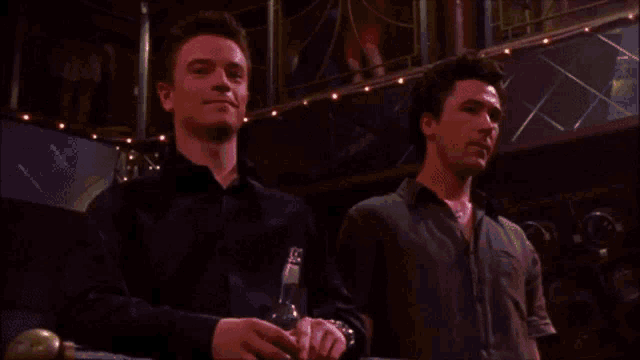 two men standing next to each other with one holding a bottle of beer