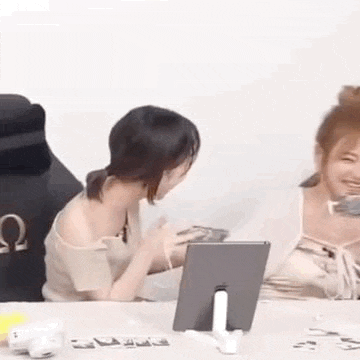 two women are sitting at a table with a tablet and a picture frame .