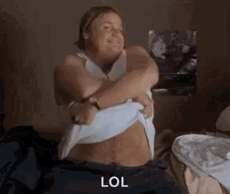 a woman is sitting on a bed taking off her shirt and making a funny face .