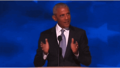 a man in a suit and tie stands at a podium speaking into a microphone