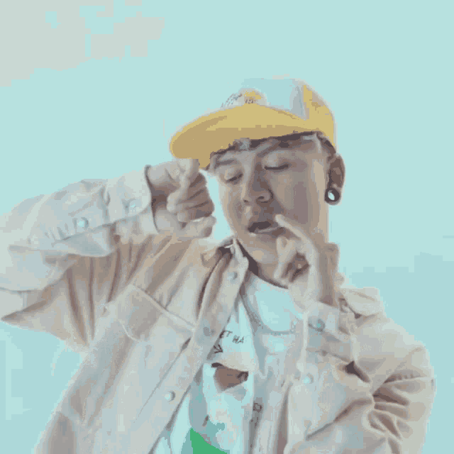 a young man wearing a yellow hat and a white shirt is covering his face