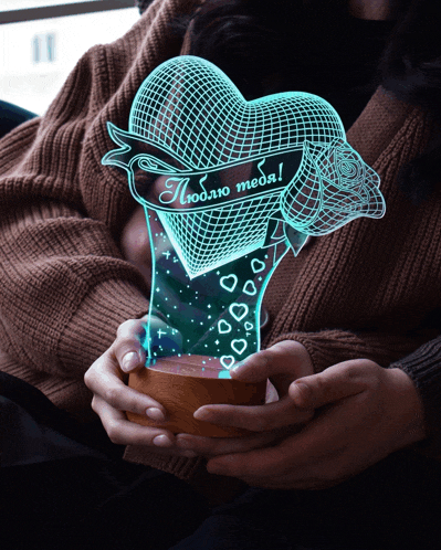 a woman is holding a heart shaped lamp that says люблю тебя