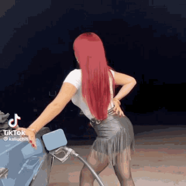 a woman with red hair is standing next to a car and holding a gas pump .