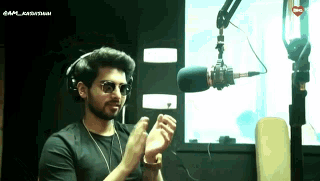 a man wearing headphones and sunglasses is clapping his hands in front of a microphone