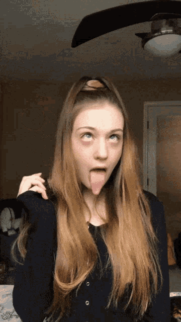 a girl with long hair sticking her tongue out in front of a ceiling fan