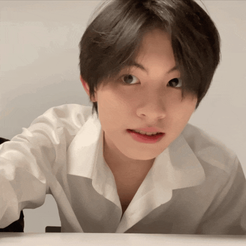 a young man wearing a white shirt looks at the camera