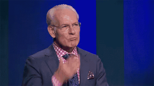 a man wearing glasses and a suit is clapping his hands .