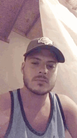 a man with a beard wearing a hat and a blue tank top .