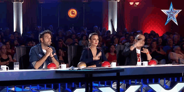 three people sitting at a table in front of a crowd with a star in the back
