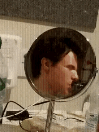 a man is looking at himself in a small mirror .