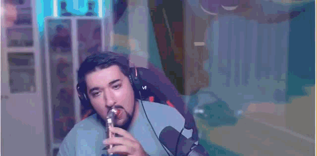 a man wearing headphones is drinking a can of pepsi while sitting in front of a microphone .