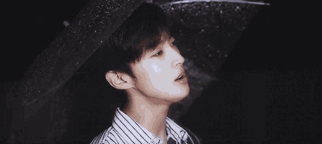 a young man in a striped shirt is holding an umbrella over his head in the rain .