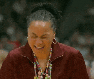 a woman wearing a maroon jacket and earrings has a necklace with the letter b on it