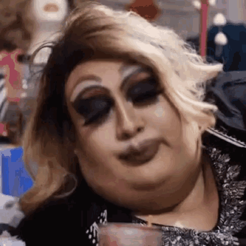 a drag queen is making a funny face while holding a candle in her hand .