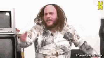 a man with long hair and a beard is standing in front of a tv .