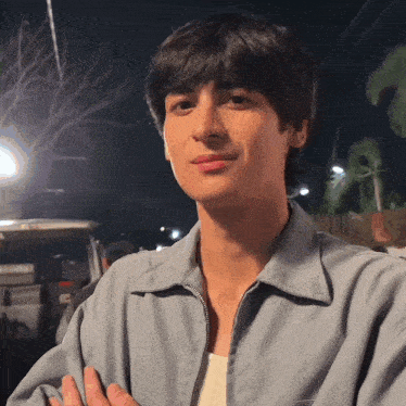 a young man in a blue jacket looks at the camera with his arms crossed
