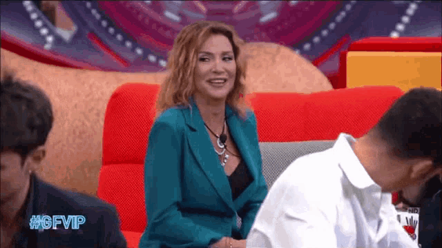 a woman in a blue suit sits on a red couch in front of a screen that says #gfvip on it