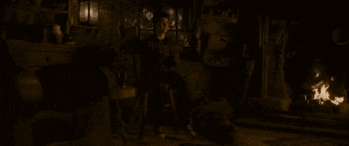 a man sits in a dark room with a fireplace in the background