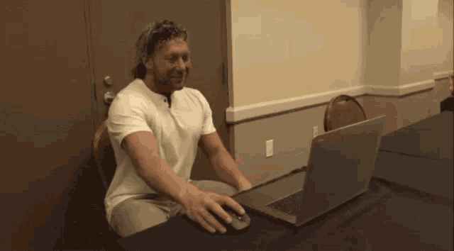 a man in a white shirt is sitting at a table using a laptop