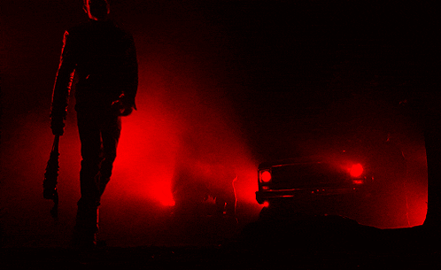 a man is holding a bat in front of a car in the dark