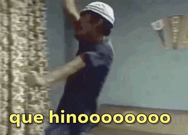 a man in a white hat is standing in front of a wall with the words que hinoooooo written in yellow