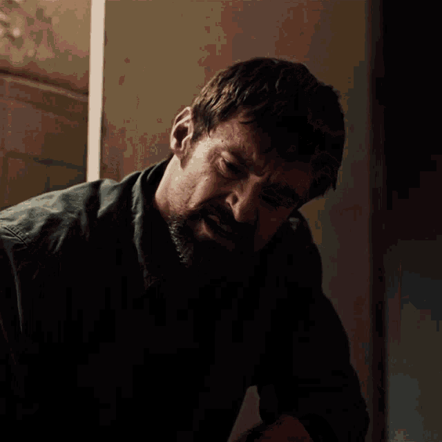 a man with a beard in a dark room looks up at something