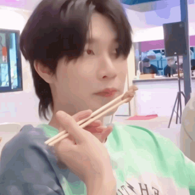 a person wearing a green shirt with a lightning bolt on it eating with chopsticks