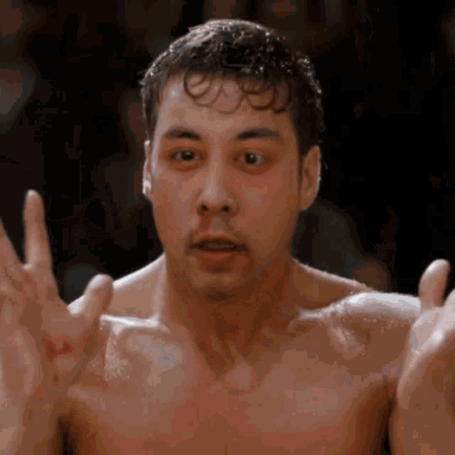 a shirtless boxer with a bloody nose holds his hands up