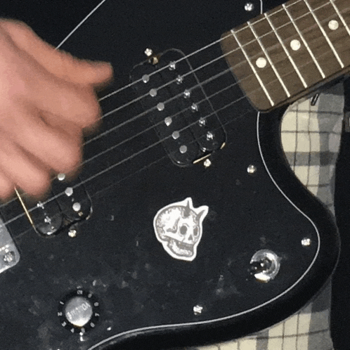 a person is playing a black guitar with a skull sticker on the neck