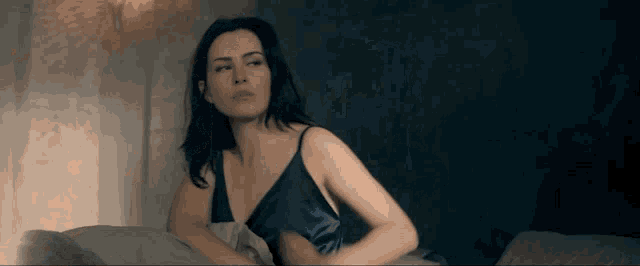 a woman in a blue slip is sitting on a bed looking at the camera
